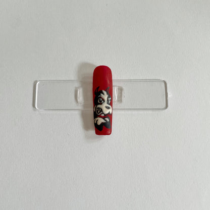 A set of custom nails with a red, white, and black design, featuring a character illustration.